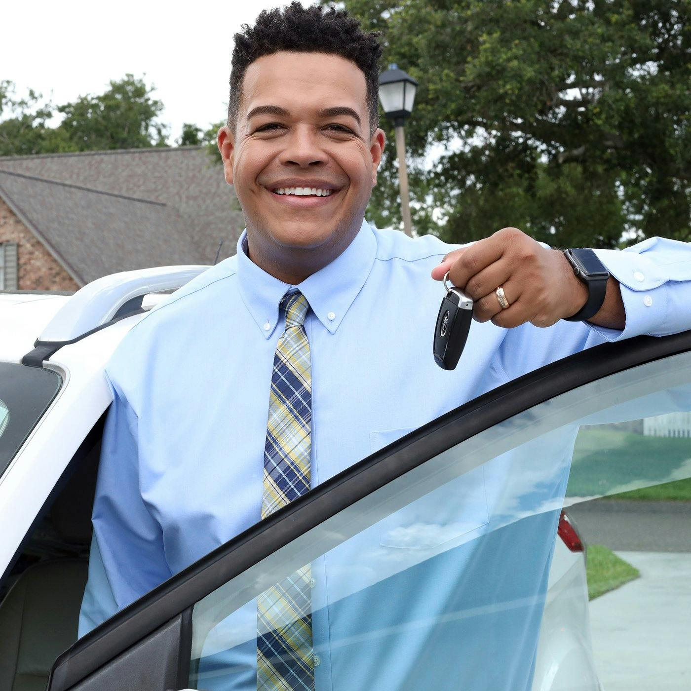 A smiling man holding a pair of keys with his car