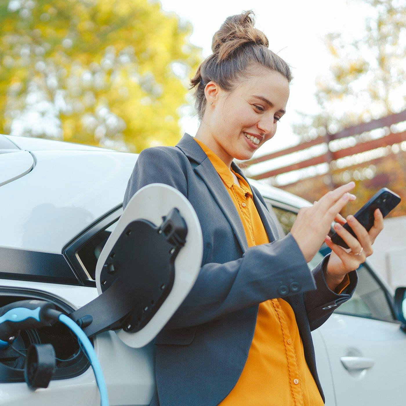 A woman uses her phone while leaning against her electric vehicle